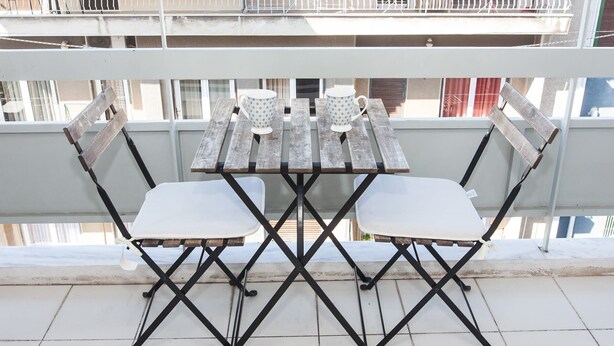 A balcony with a wooden table and two chairs, a white cushion on each chair, and a white mug on the table. - Fabulous apartment at Exarcheia (Athens)