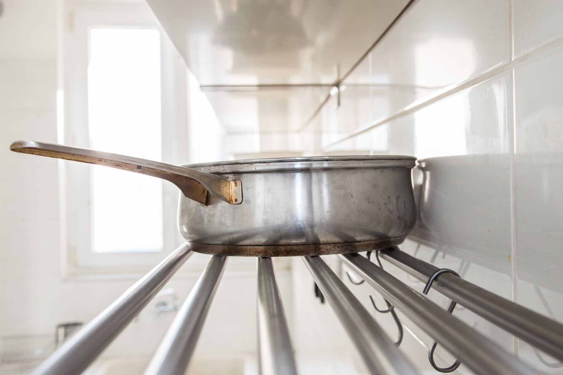Una pentola d'acciaio inossidabile su un ripiano in una cucina con pareti piastrellate in bianco e una finestra.