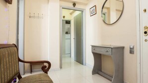A hallway with a wooden chair, a small console table, a mirror, and a door leading to a kitchen. - Fabulous apartment at Exarcheia (Athens)