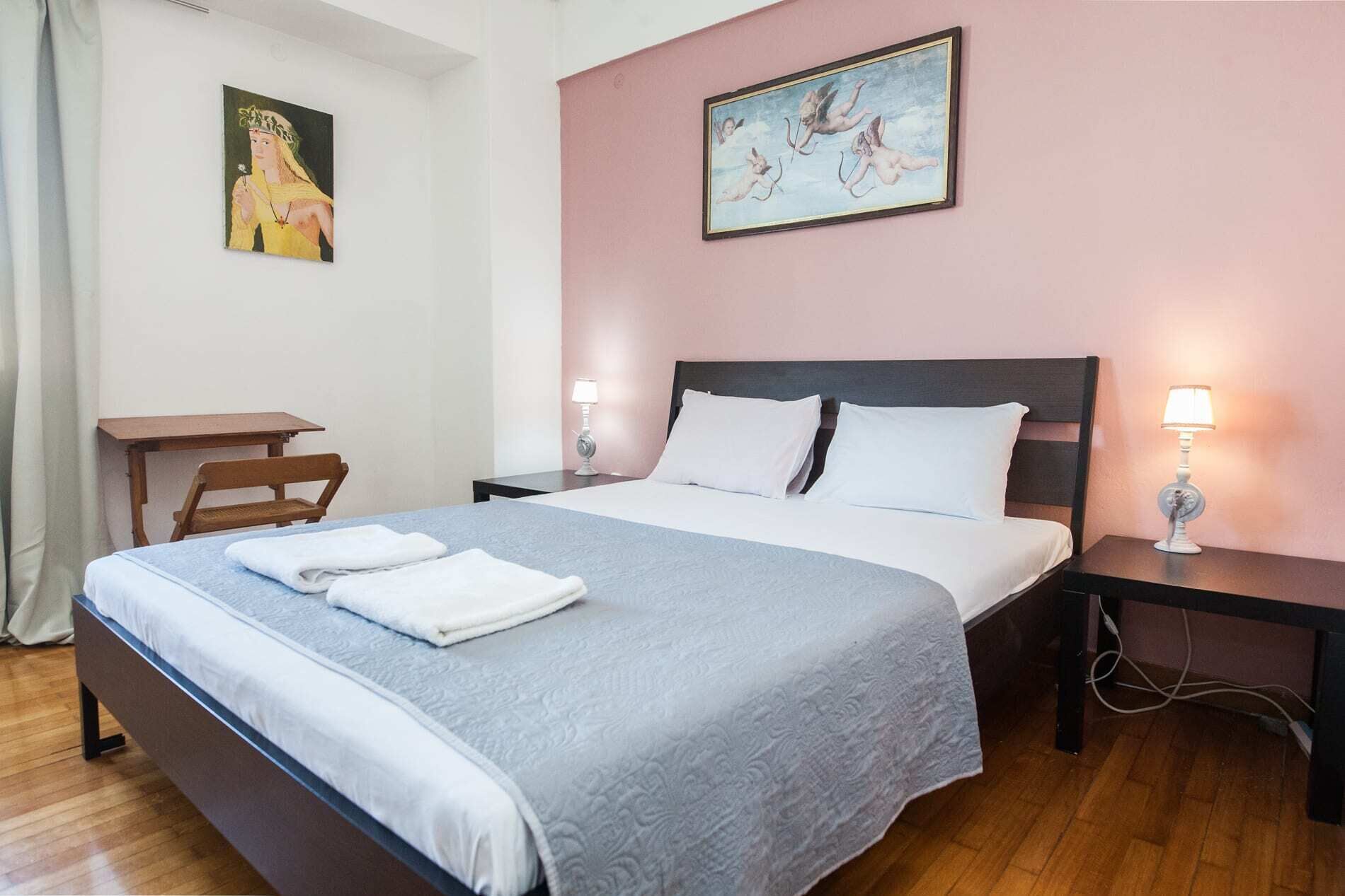 A neatly made bed with white and gray linens, two bedside lamps, a wooden nightstand, and a small table with a chair.