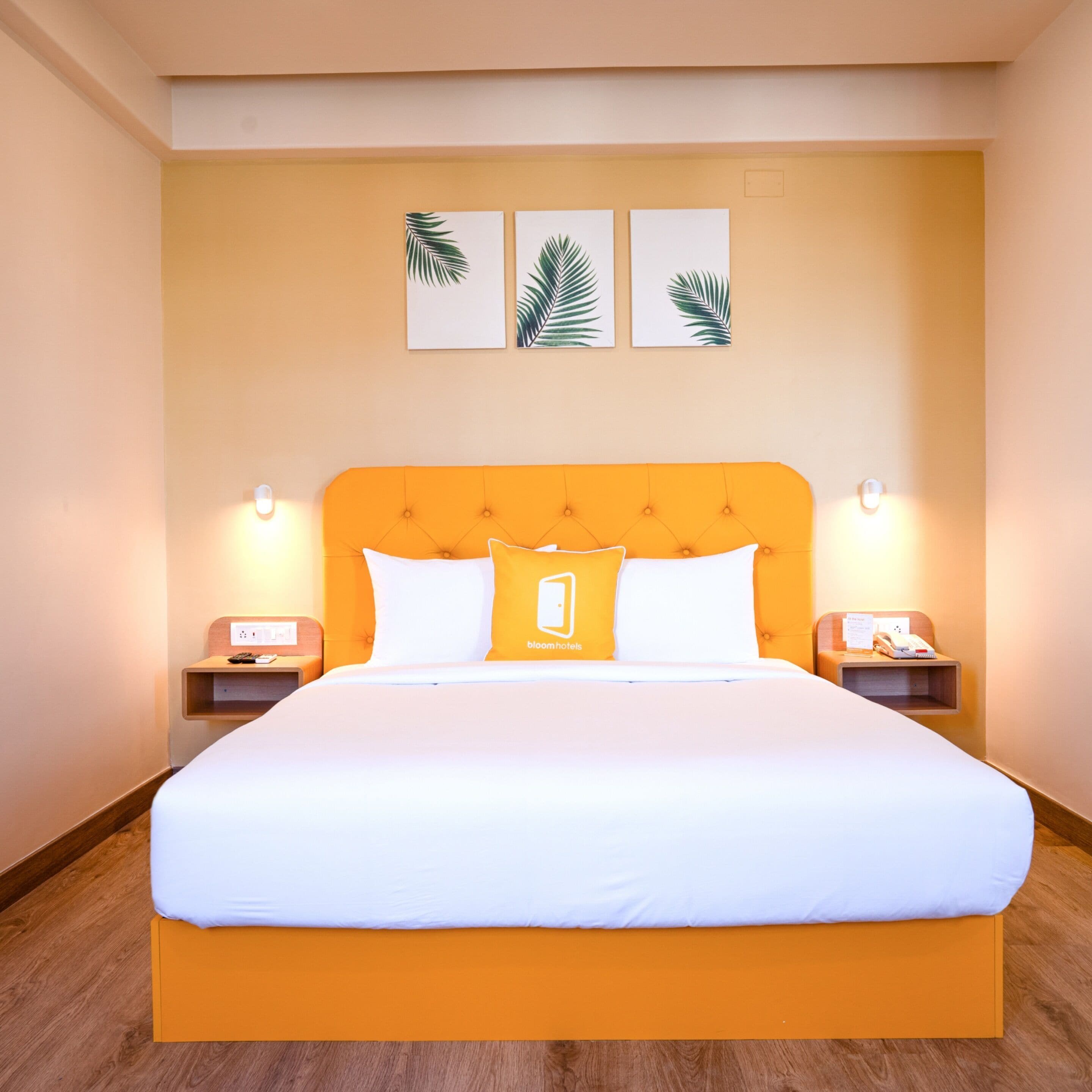 Una habitación de hotel con una cama grande, dos mesitas de noche y tres piezas de decoración de hojas enmarcadas.