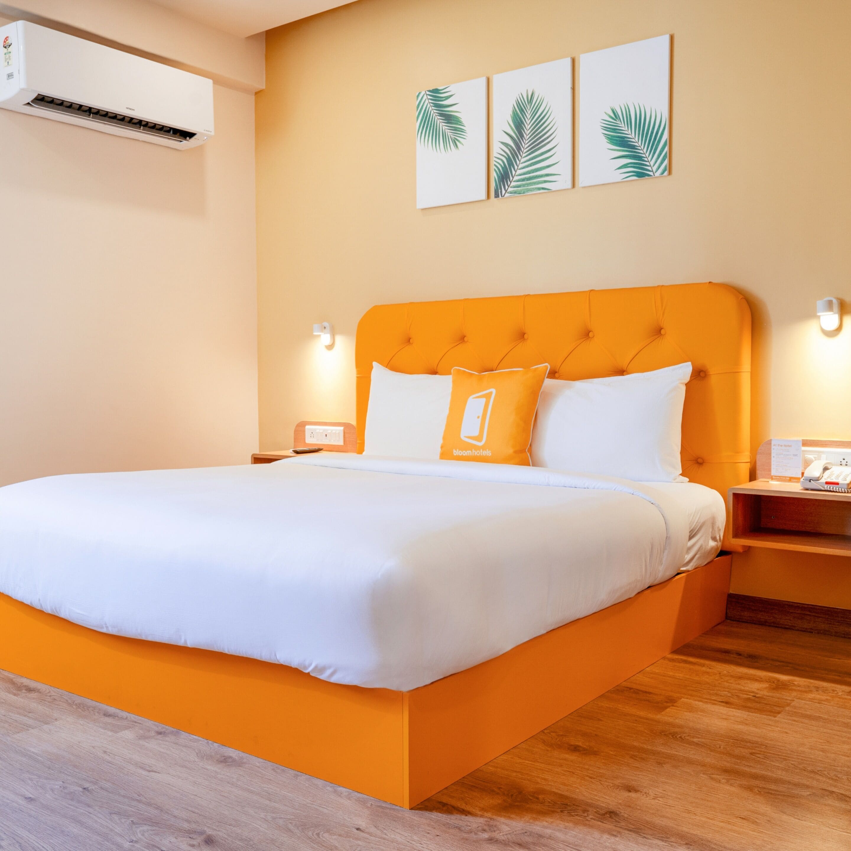 A hotel room with a large bed, an air conditioner, a nightstand with a phone, and wall art.