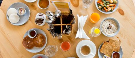 A breakfast spread on a round wooden table with various dishes including pancakes, omelettes, toast, and a variety of beverages.