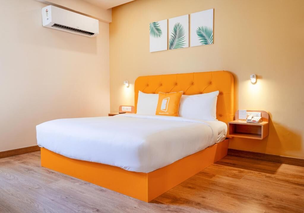 Une chambre d’hôtel équipée d’un lit, d’un appareil de climatisation, d’une table de chevet et d’une étagère fixée au mur.