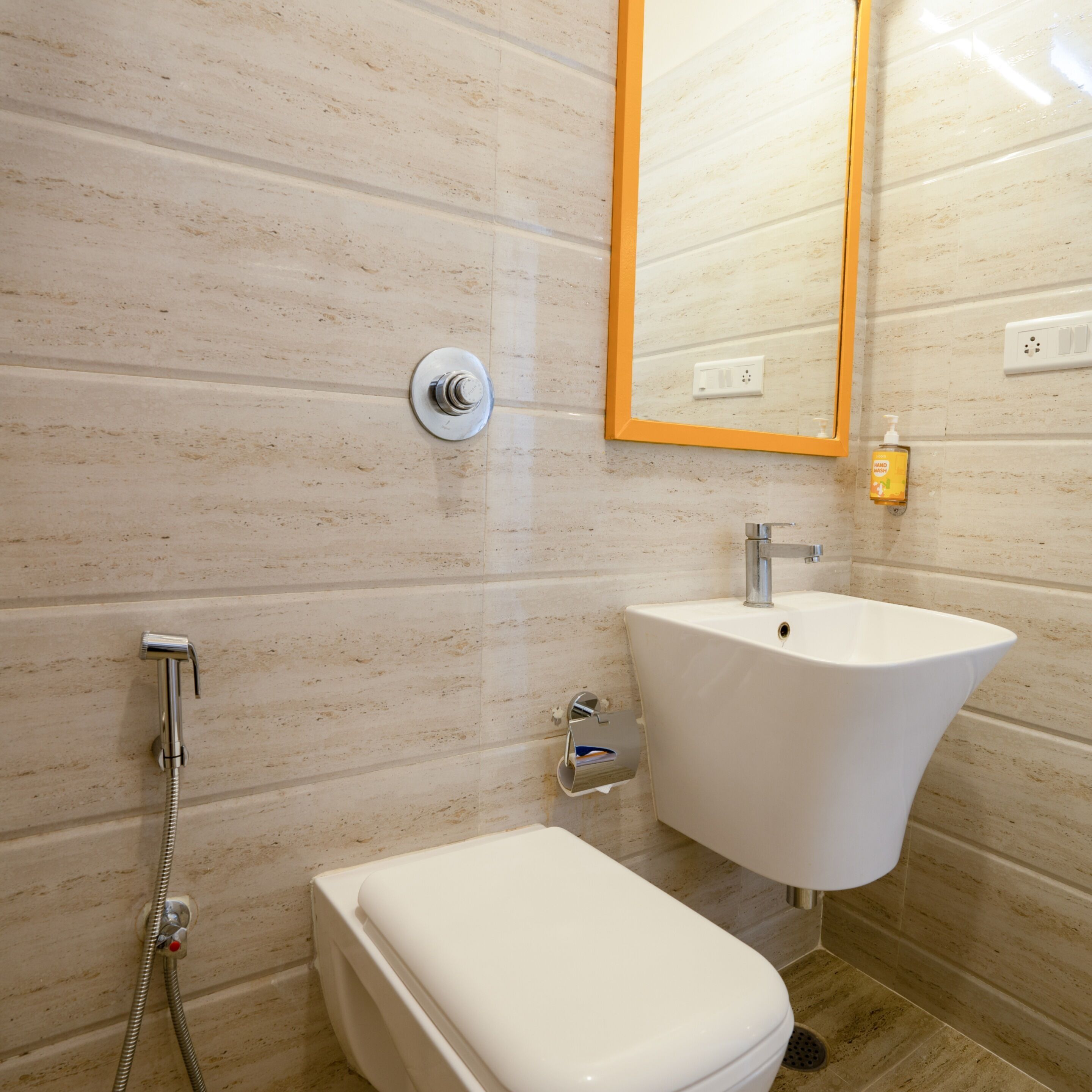 Un baño con un lavamanos blanco, un espejo con marco naranja y una ducha.