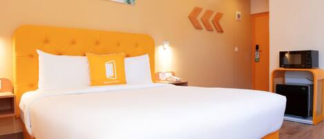 A hotel room with a large bed, a bedside table, a nightstand, a microwave, and a door with a sign.
