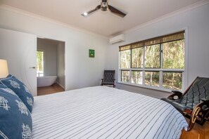 A bedroom with a bed, a chair, a window with a view, a ceiling fan, and an air conditioning unit.