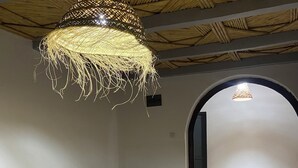 Ein Zimmer mit einer gewebten Pendelleuchte, einer Holzbänkl mit Kissen und einem gemusterten Boden.