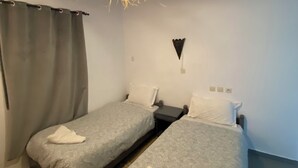 Ein Zimmer mit zwei Betten, einer Hängelampe und einem Vorhang.