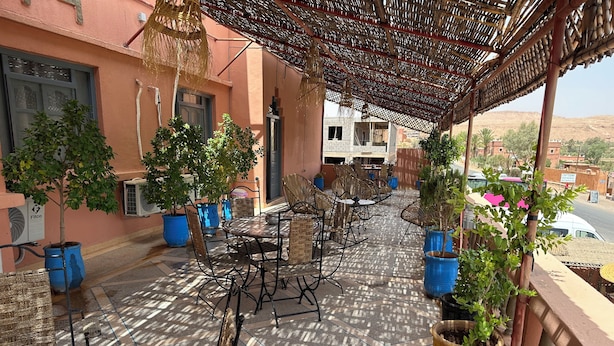 Eine Terrasse im Freien mit Korbmöbeln, Blumentöpfen und einem gemusterten Boden.