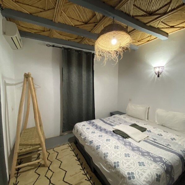 A bedroom with a bed, a hanging light fixture, a wall-mounted light, a window with curtains, and a wooden ladder.