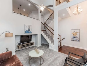 A spacious living area with a fireplace, a staircase, and a chandelier.