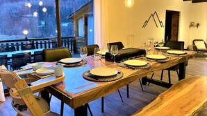 Zona de menjador amb una taula de fusta llarga preparada per a sis persones, amb caires al voltant i vista a un paisatge nevós a través de grans finestres.