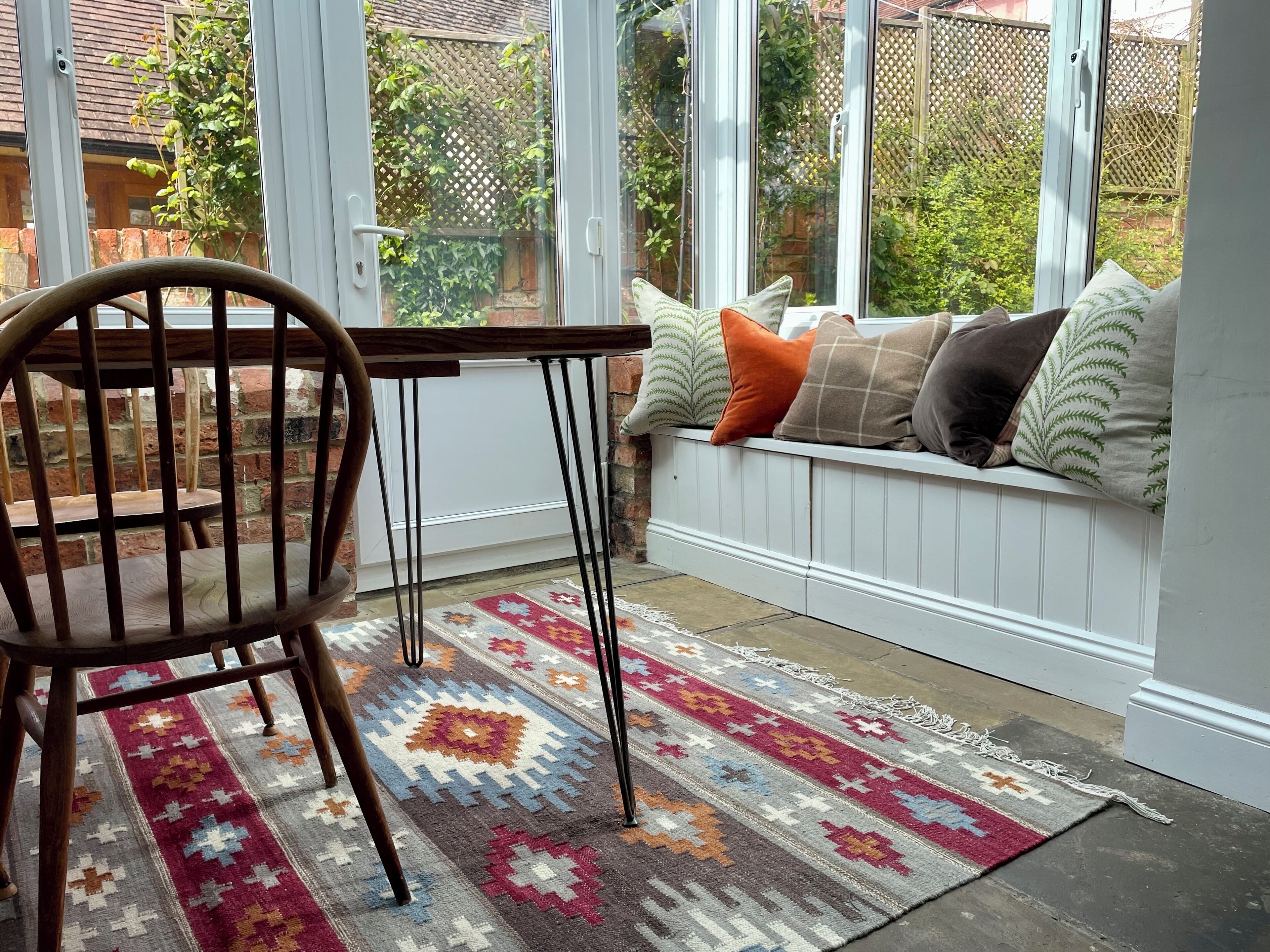 A cozy seating area with a bench, a wooden chair, and a patterned rug.