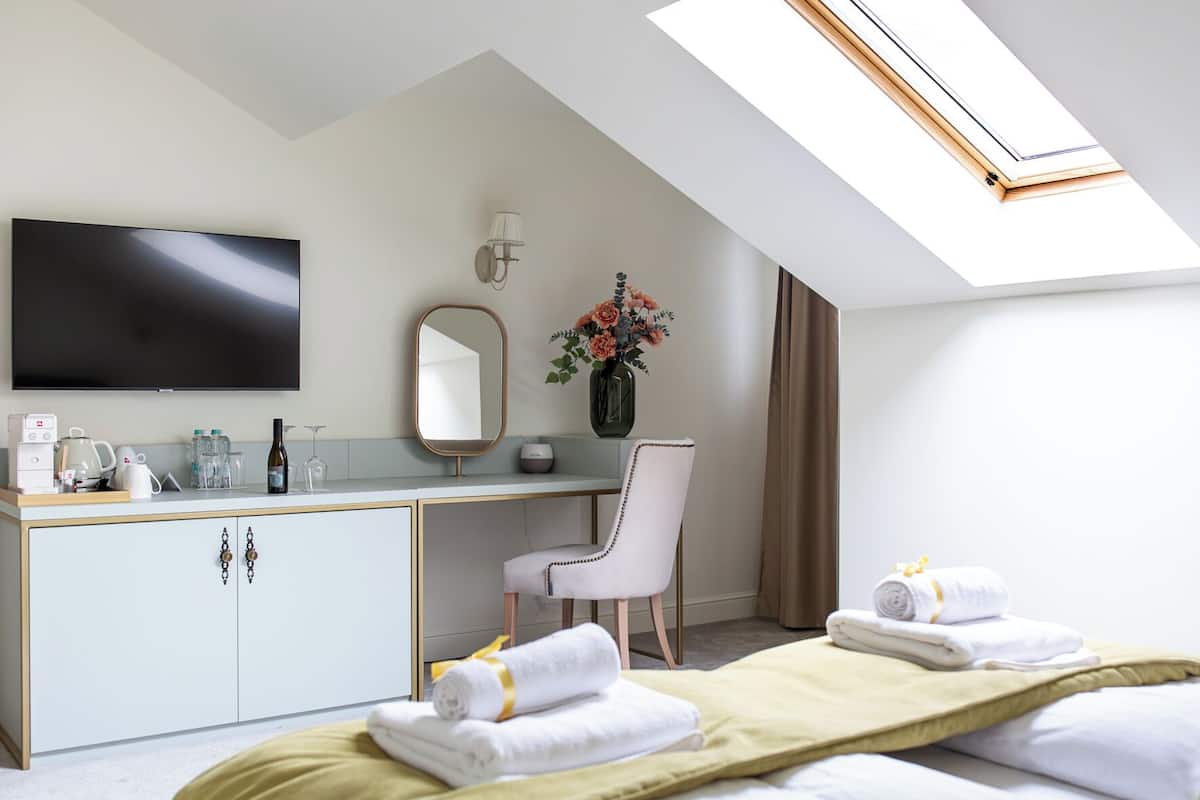 Une chambre d’hôtel moderne équipée d’une grande télévision, d’un bureau avec un miroir, d’un vase avec des fleurs et de deux lits avec des serviettes.