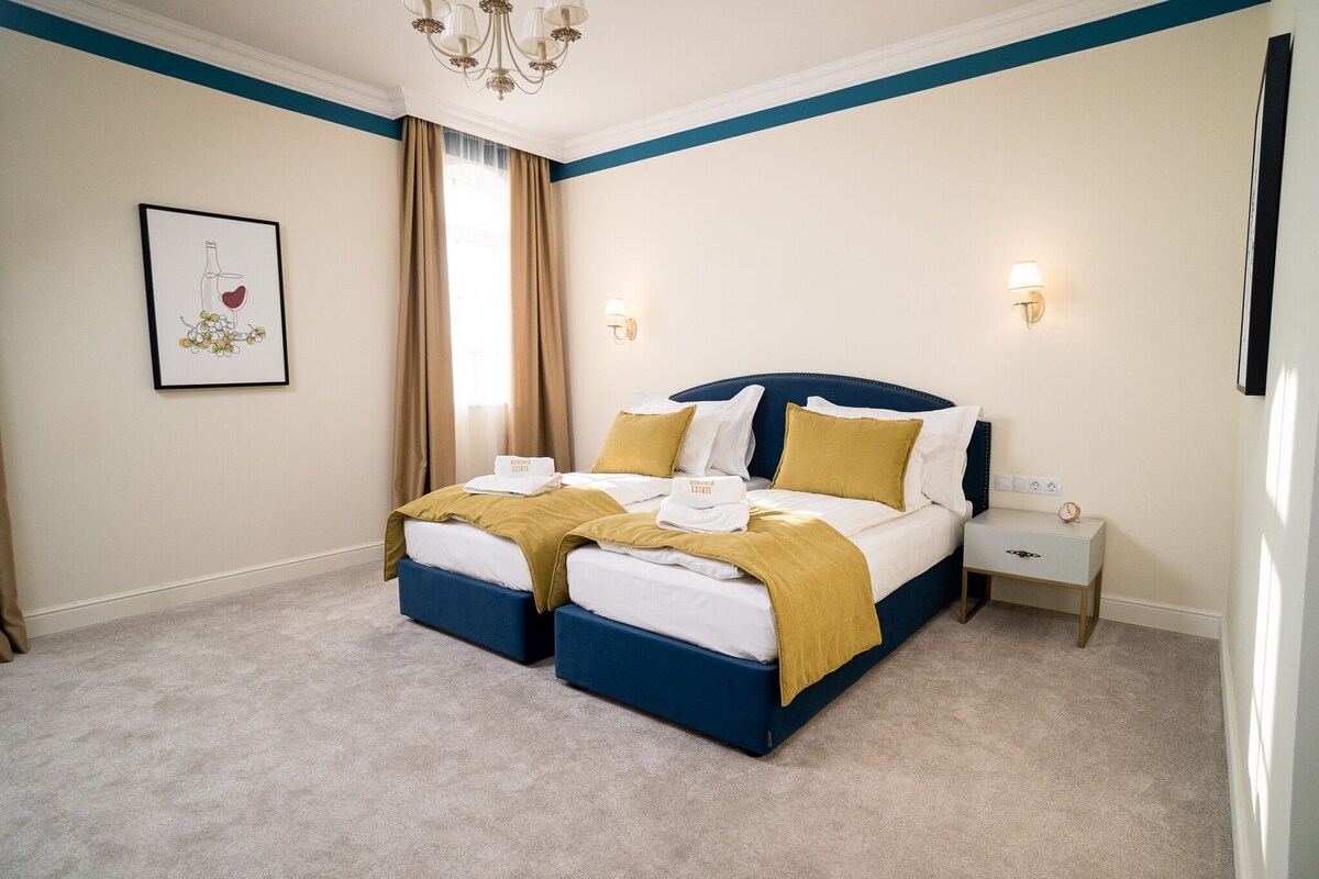 Un lit double avec une tête de lit bleue, deux tables de chevet, une commode, un tableau encadré au mur et un lustre.