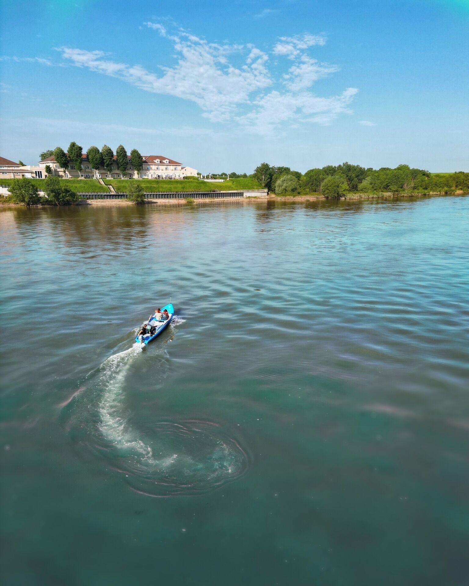 Un río tranquilo con una embarcación azul dejando una estela.