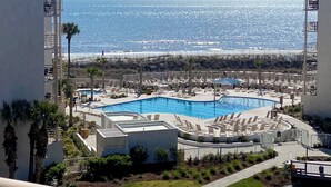 Un complexe hôtelier doté d’une piscine centrale, de chaises longues et offrant une vue sur l’océan.