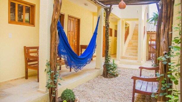 Un espacio al aire libre cubierto con una hamaca, sillas de madera y una escalera que lleva a un nivel superior.