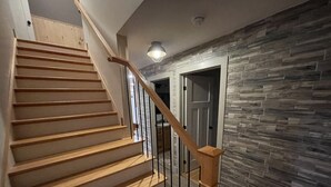 A wooden staircase with a glass railing leading to a room with a stone wall.