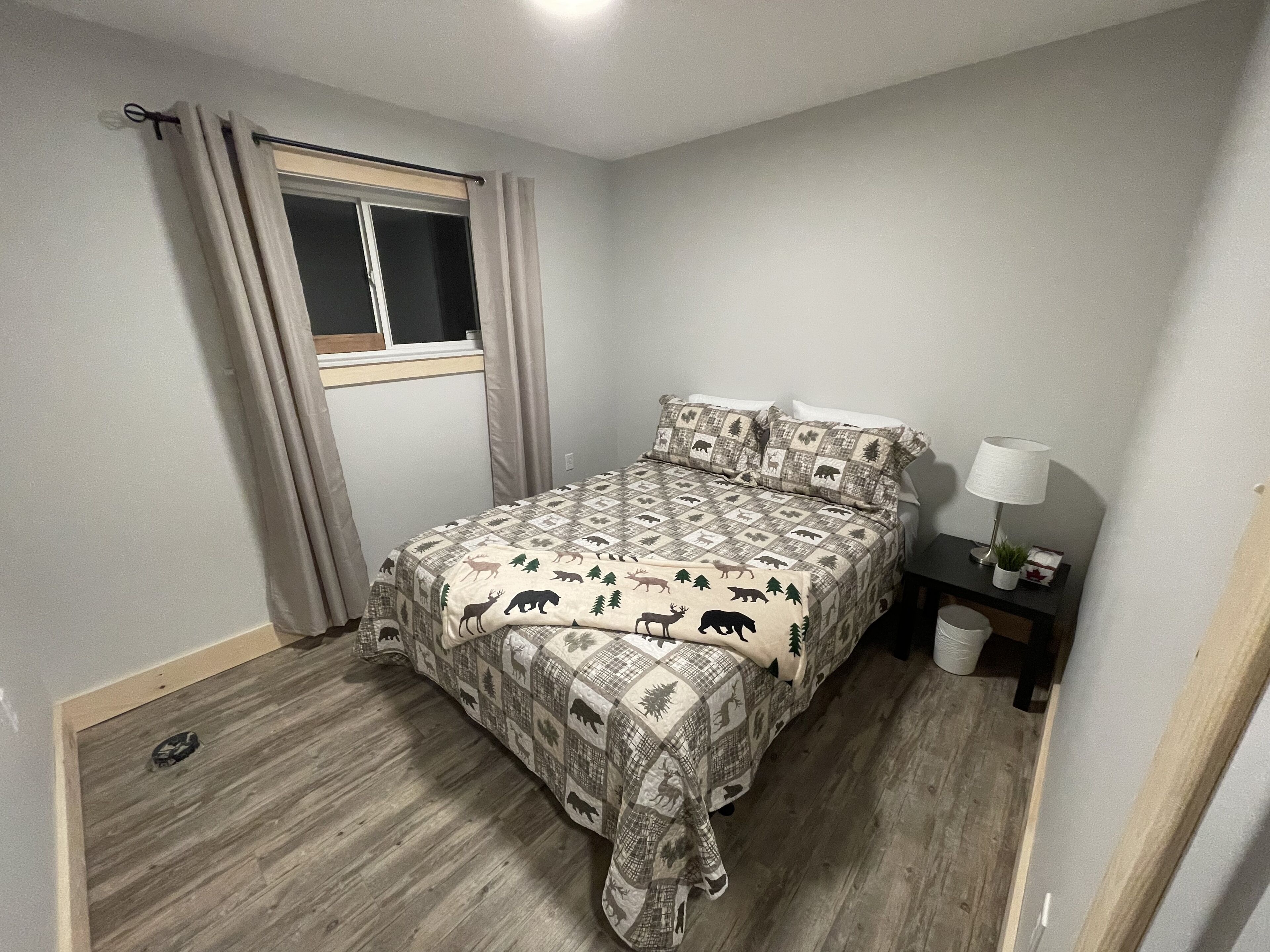 A bedroom with a bed, a window with curtains, a bedside table with a lamp, and a small plant.