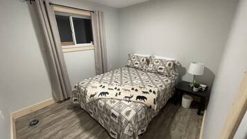 A bedroom with a bed, a window with curtains, a bedside table with a lamp, and a small plant.