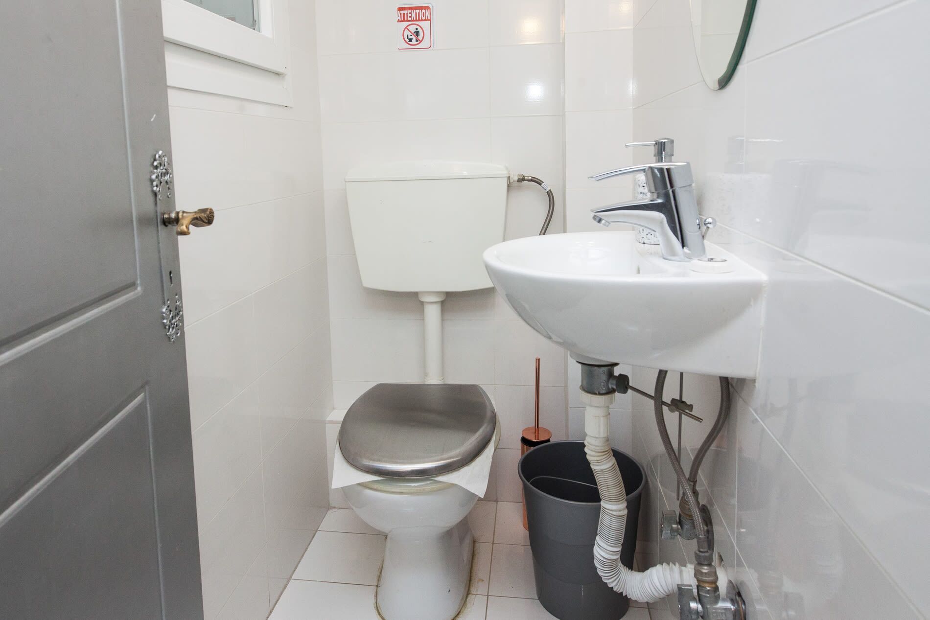 A small, clean bathroom with a toilet, sink, and a trash bin.