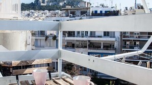 A rooftop terrace with wooden benches and two pink mugs, overlooking a cityscape with buildings and a hill. - Gorgeous 2 bedrooms apt at Exarcheia (Athens)