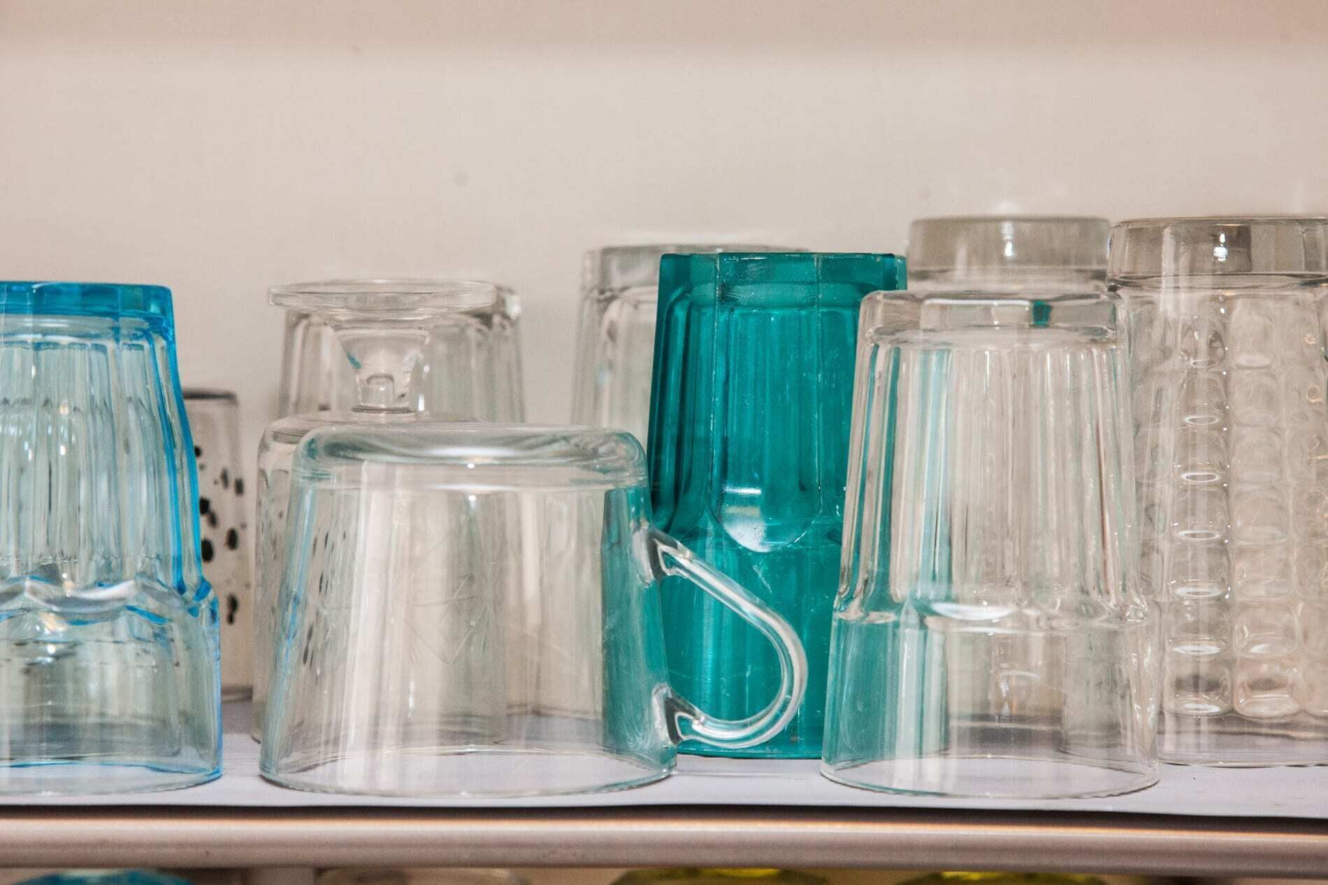A shelf with various glass containers, including a teal-colored pitcher and several clear glass mugs.
