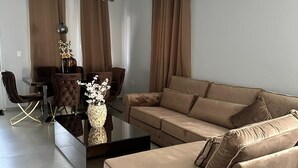 A modern living room with a beige sofa, a glass coffee table, and a dining area with a table and chairs. - Beautiful detached home with pool and gym! (Willemstad)