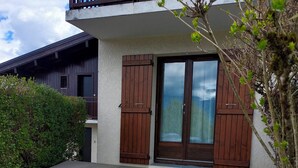 A two-story building with a wooden deck and stone border. - Studio-cabin apartment (Combloux)