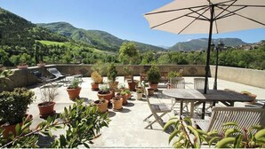 Una terraza en la azotea con plantas en macetas, mobiliario exterior y vistas a un paisaje montañoso.