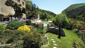 Un edificio de piedra con jardín, piscina y puente de piedra.