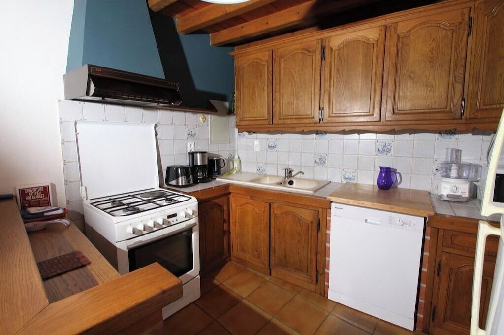 A compact kitchen with wooden cabinets, a white stove, a dishwasher, and a tiled backsplash.