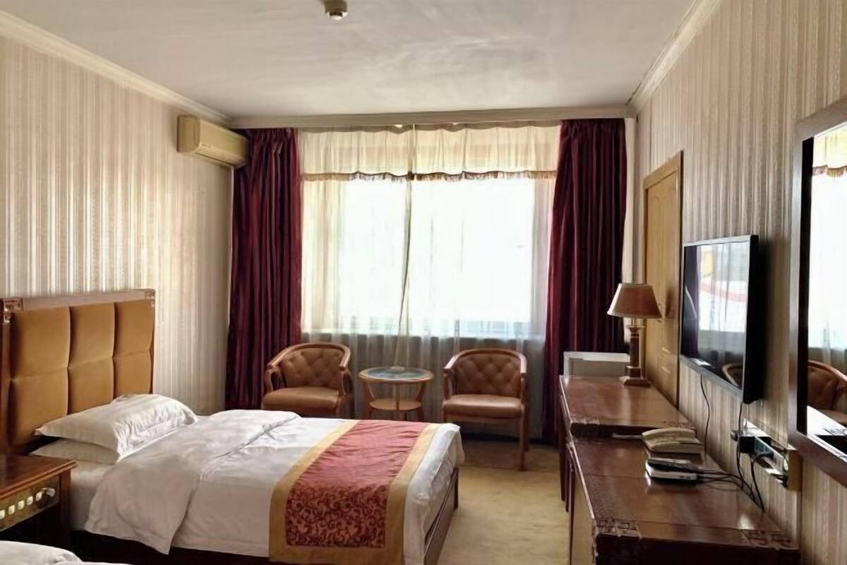 Una habitación de hotel con una cama, dos sillones, una mesita redonda, un escritorio con lámpara, televisión y un espejo grande.