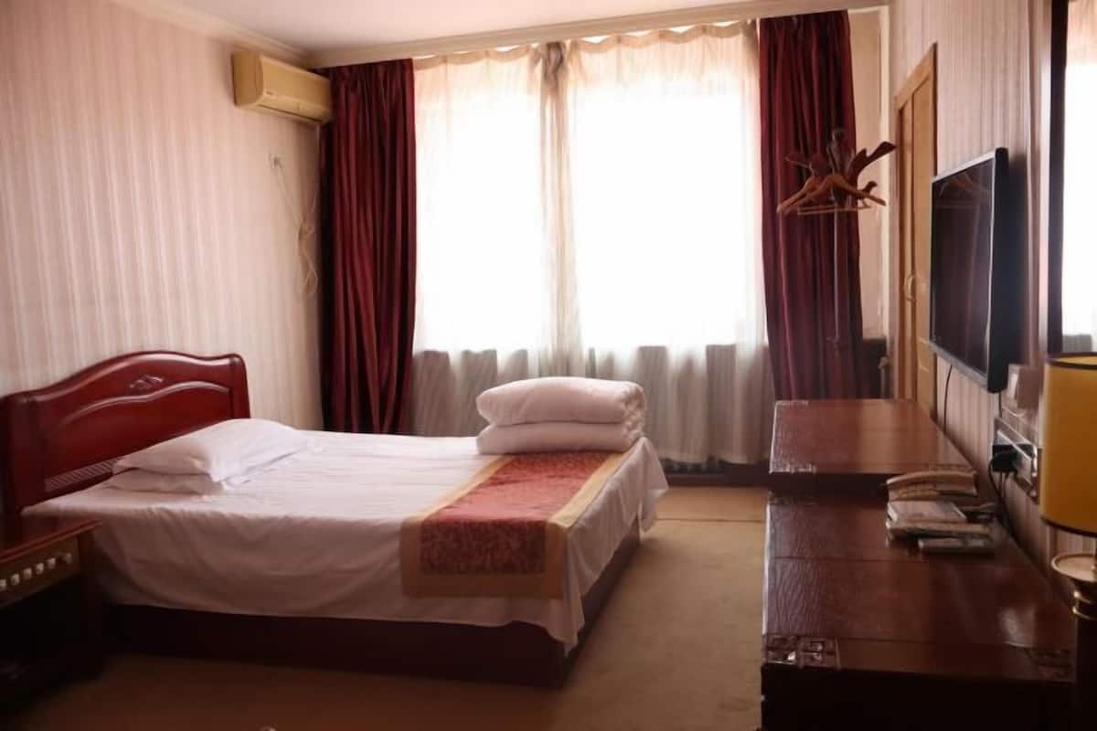 Habitación de hotel con cama, escritorio, televisor y ventana con cortinas.