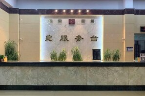 Una recepción con encimera de mármol, un cartel con caracteres chinos y plantas en macetas.