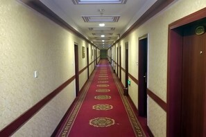 A hotel hallway with a red carpet, doors on both sides, and a ceiling with recessed lighting.