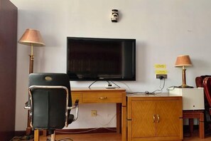 Una habitación con escritorio de madera, una silla negra, televisor montado en la pared y dos lámparas.