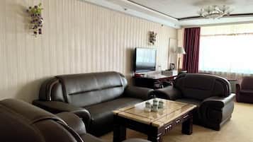 A modern living room with leather sofas, a glass coffee table, a flat-screen TV, and decorative plants.