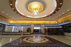 Un vestíbulo de hotel con un emblema circular central, una recepción y una amplia entrada.