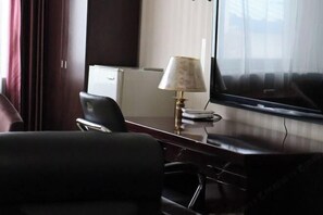 Habitación de hotel con escritorio, una silla, lámpara, televisor y ventana con cortinas.