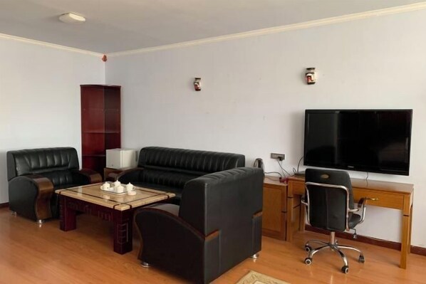 Ein Wohnzimmer mit schwarzem Ledersofa, einem Holztisch, einem Fernseher und einem Schreibtisch mit Stuhl.
