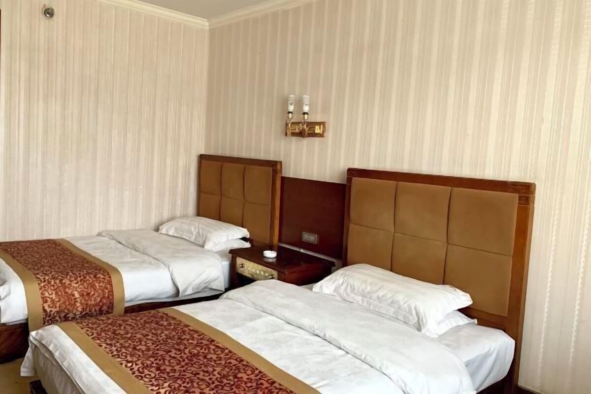 Habitación de hotel con dos camas, una mesita de noche y una lámpara fijada a la pared.