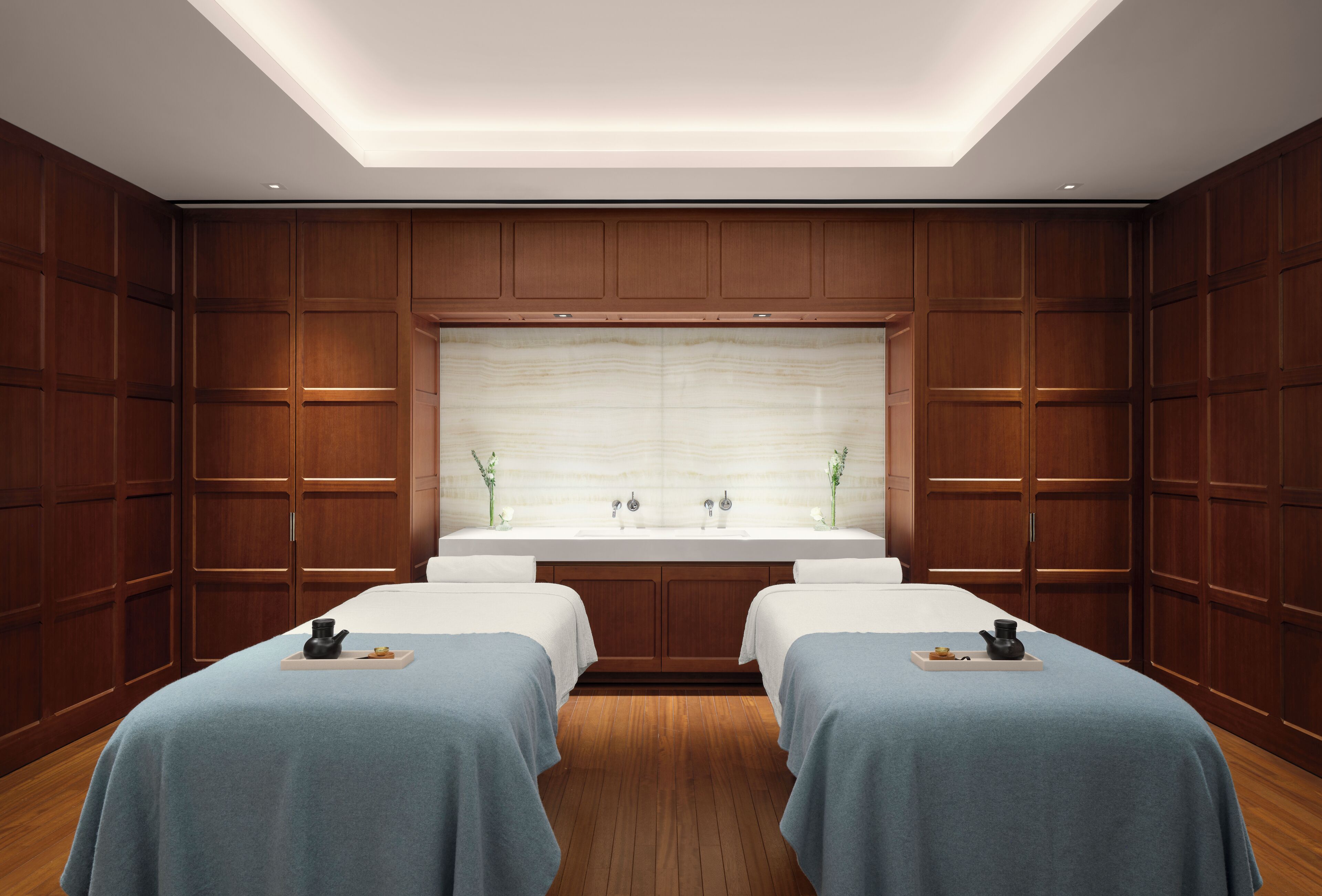 A hotel room with a wooden panel wall, a large mirror, and two beds with blue bedspreads.