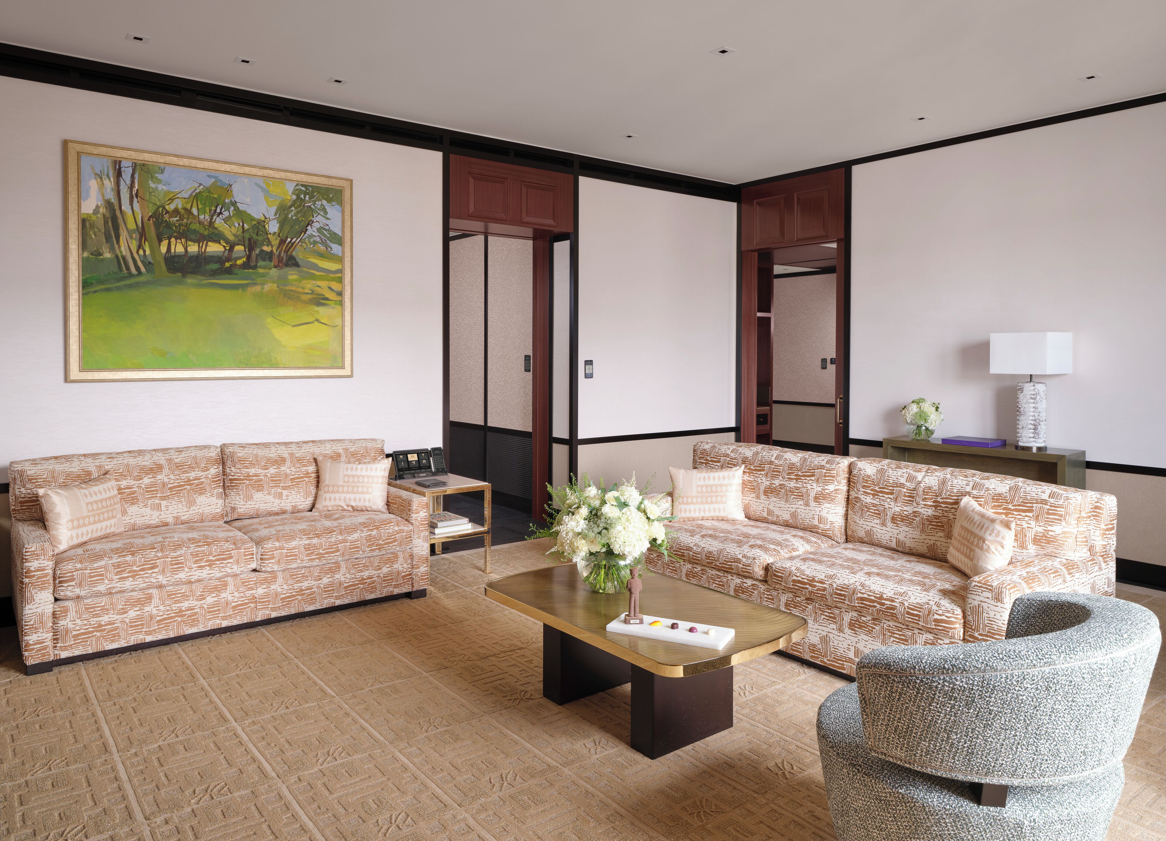 A living room with two patterned sofas, a coffee table, a side table, a painting, and a lamp.