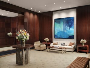 A modern lobby with a large abstract painting, a round table with a vase of flowers, a sofa, and a bench. - The Peninsula London (London)
