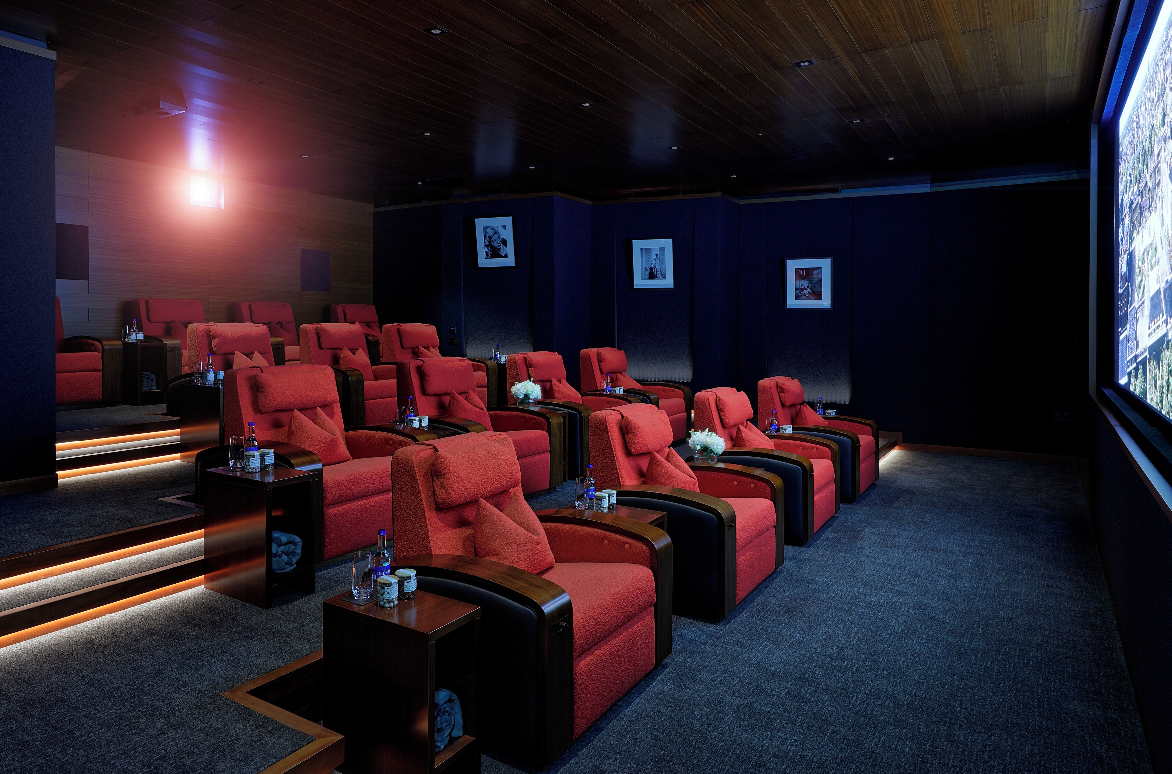 A cinema with rows of red seats, wooden floors, and framed pictures on the walls.