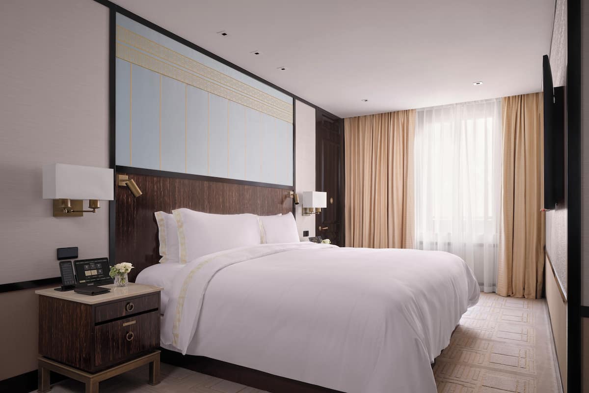 A modern hotel room with a large bed, bedside tables, a nightstand, and a large mirror.