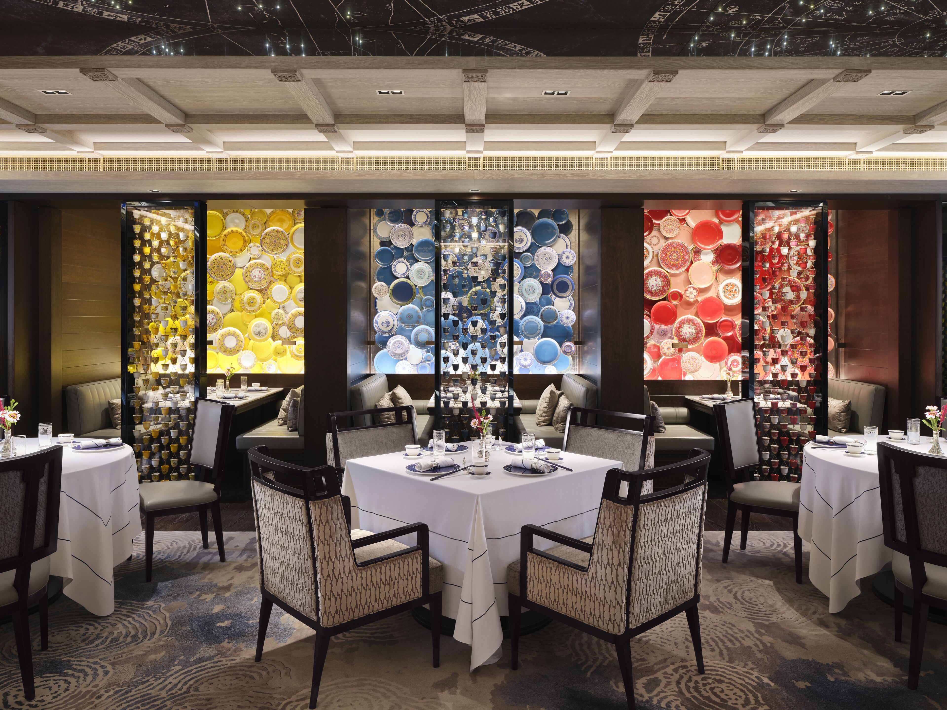 A dining area with round tables and chairs, a patterned carpet, and a wall decorated with plates.